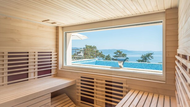 Un sauna avec des parois en bois, un banc et une fenêtre donnant sur une piscine et un paysage.