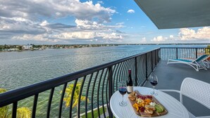 A balcony with a table set for a meal, overlooking a body of water and a distant shoreline. - FUSION Resort Waterfront Suites (Treasure Island)