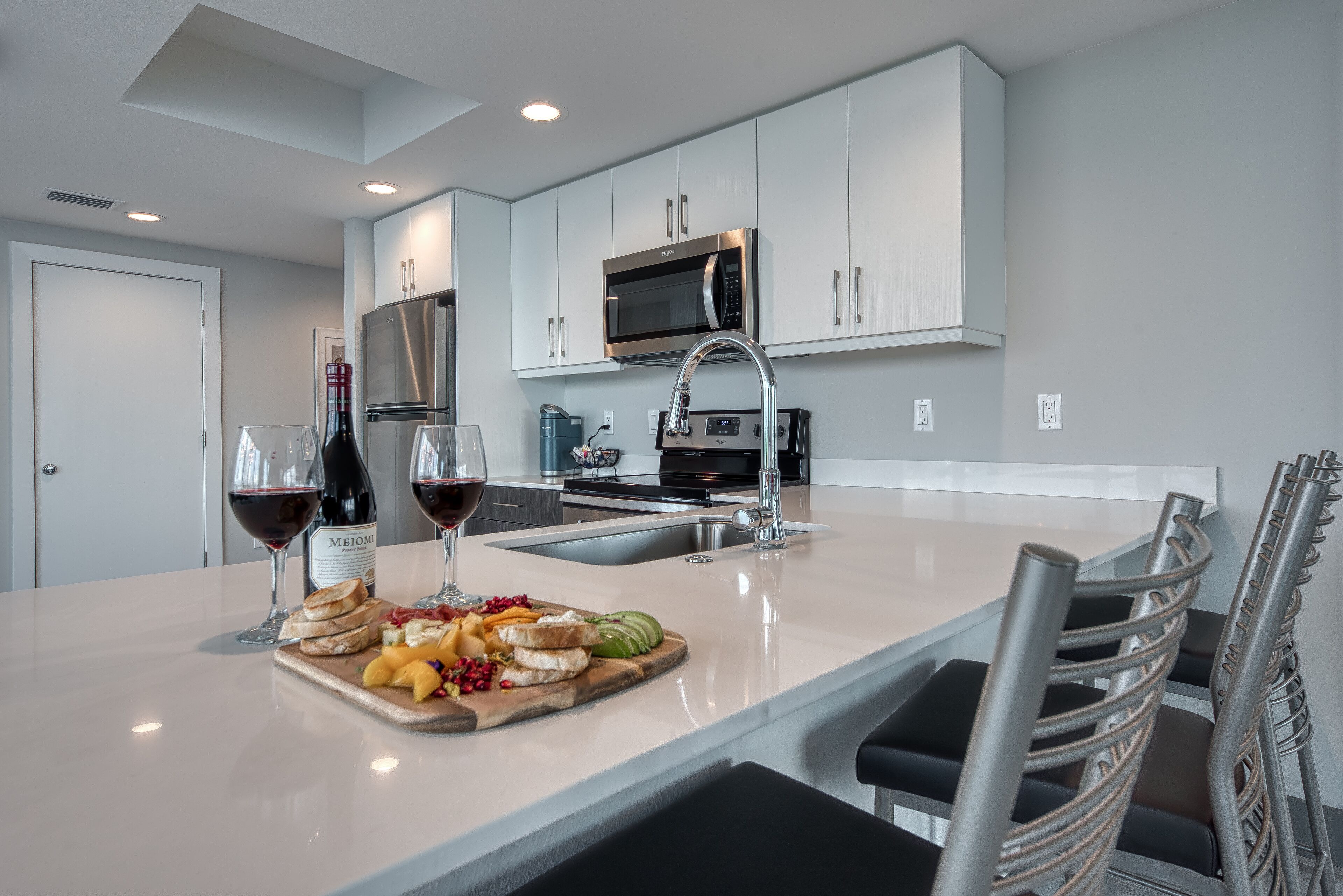 A modern kitchen with a central island, stainless steel appliances, and a seating area with metal chairs.