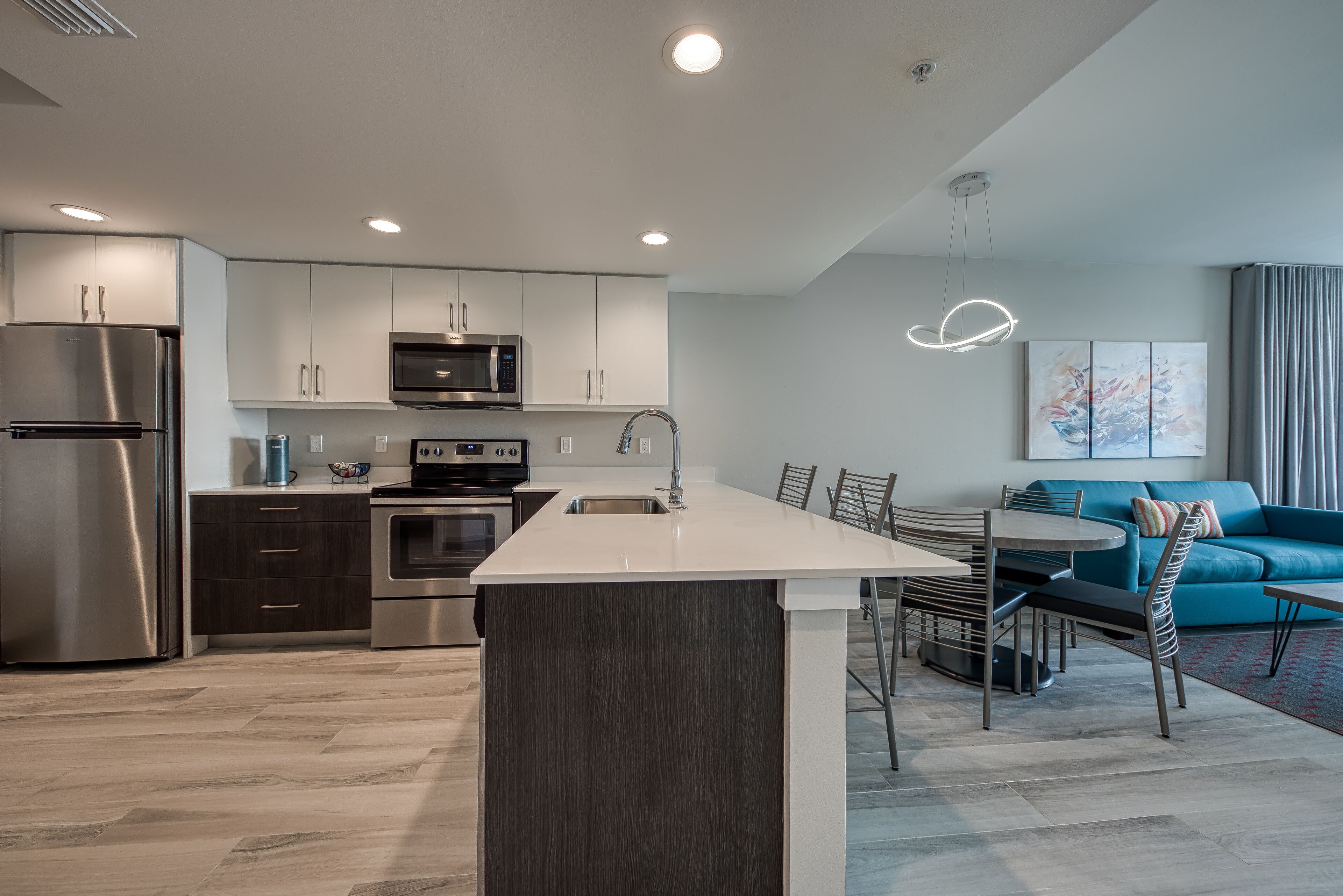 A modern kitchen with a central island, stainless steel appliances, and a dining area with a blue sofa.
