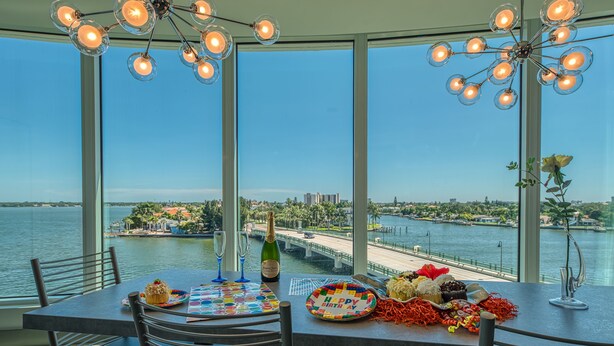 A dining table with a birthday cake, champagne, and a scenic waterfront view. - FUSION Resort Waterfront Suites (Treasure Island)