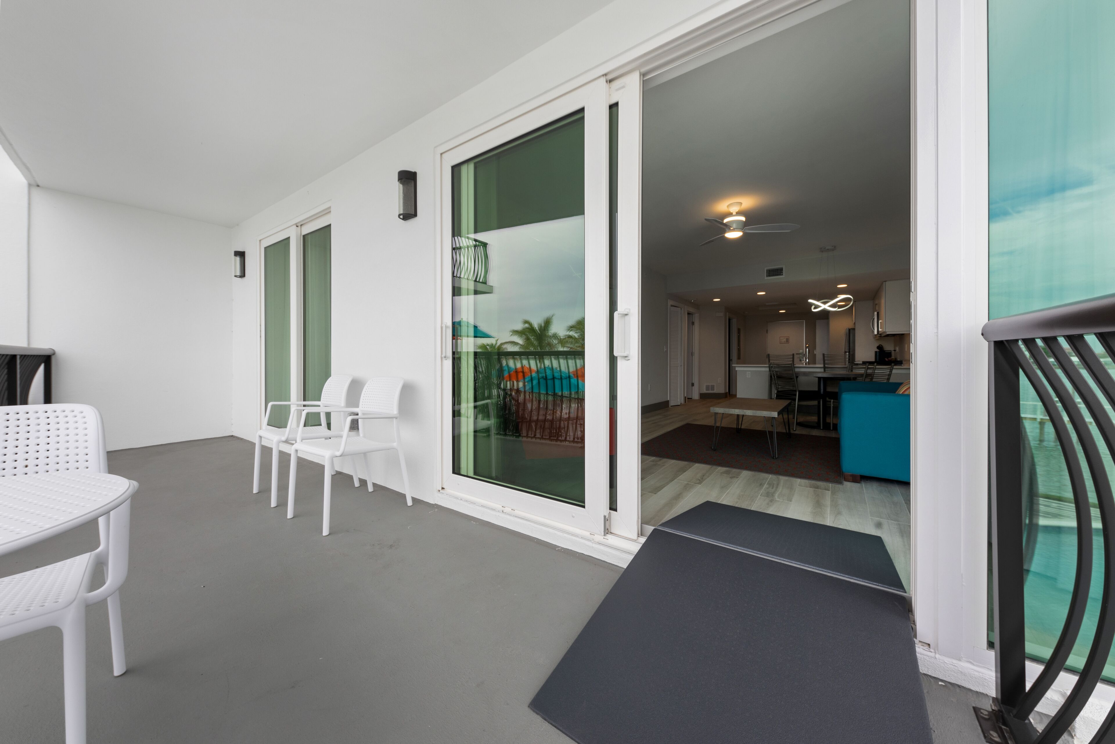 Un intérieur moderne avec un balcon, des meubles blancs et un coin cuisine visible à travers des portes vitrées.