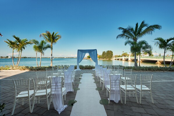 An outdoor wedding aisle with white chairs and a draped arch, overlooking a body of water. - FUSION Resort Waterfront Suites (Treasure Island)