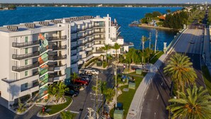 A modern multi-story hotel with balconies, a parking area, and a view of the sea. - FUSION Resort Waterfront Suites (Treasure Island)