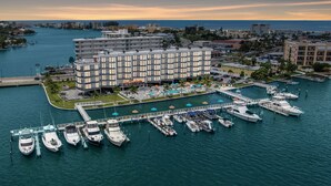 An aerial view of a marina with boats docked, a hotel with multiple floors, and a waterfront promenade. - FUSION Resort Waterfront Suites (Treasure Island)