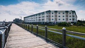 A waterfront hotel with a long wooden boardwalk leading to the building, featuring multiple balconies and a flag.