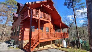 A log cabin with a balcony, a porch, and a chimney. - Cozy Log Home, Centrally Located, 2 Master Suites, Hot Tub, Game and Movie Rooms (Sevierville)