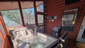 A hot tub area with a wooden deck, a small table, and a window with blinds. - Cozy Log Home, Centrally Located, 2 Master Suites, Hot Tub, Game and Movie Rooms (Sevierville)