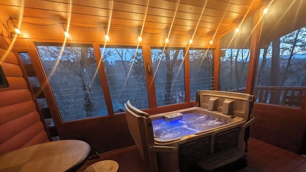 A wooden deck with a hot tub, a table, and chairs. - Cozy Log Home, Centrally Located, 2 Master Suites, Hot Tub, Game and Movie Rooms (Sevierville)