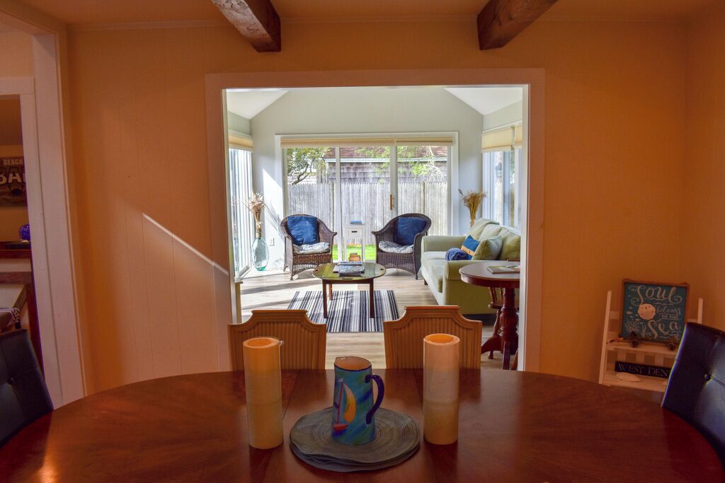 A dining area with a round table, four chairs, and three candles. There is a wicker chair and a sofa in the background.