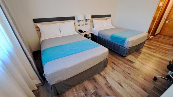 Une chambre d’hôtel avec deux lits, un plancher en bois et une table de chevet avec une lampe.