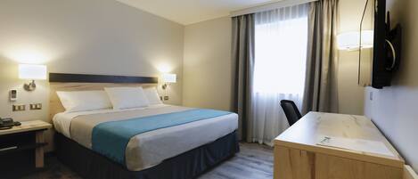 A hotel room with a bed, bedside tables, a desk, a chair, a TV, and a window with curtains.
