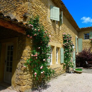 Ein Steinhaus mit rustikalem Charme, mit einem Schotterweg und rosafarbenen Rosen, die an den Wänden hochranken.