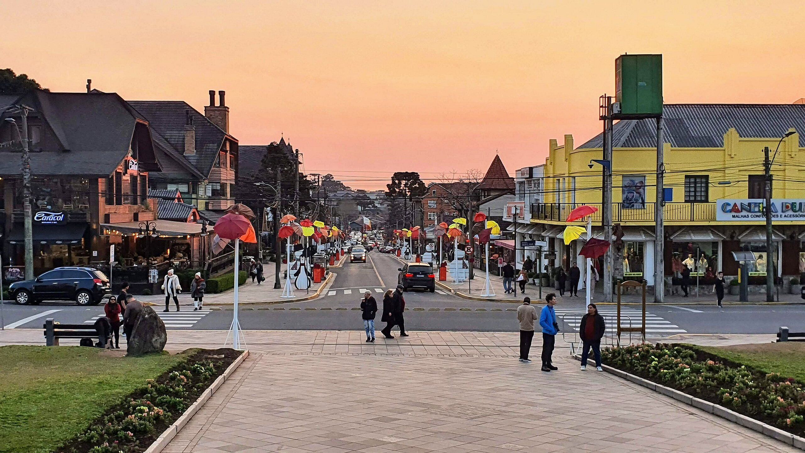 Straatbeeld bij zonsondergang met gebouwen, voetgangers en geparkeerde auto's.