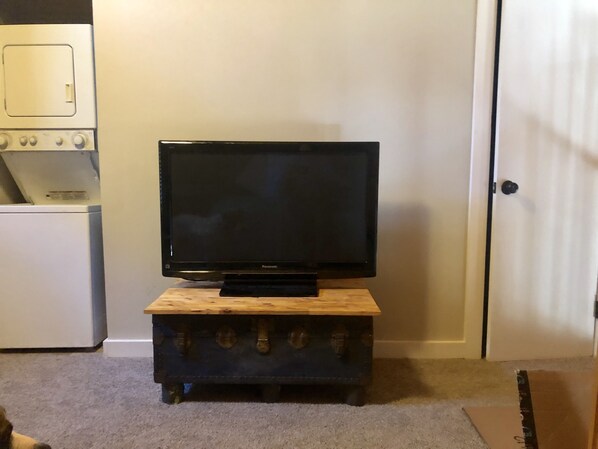 A television on a wooden stand in a room with a white door and a white appliance in the background.