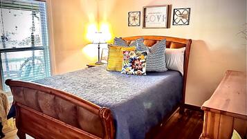 Un dormitorio con una cama de madera, una mesita de noche, una lámpara y una ventana con persianas.