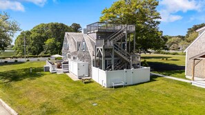 A multi-level wooden structure with a staircase, surrounded by a white fence and green grass. - Stunning Five bedroom Captain's Home sleeping 12! (West Dennis)