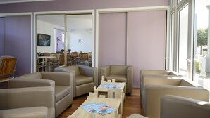 A modern lounge area with leather sofas, wooden tables, and a large window providing a view of the outdoors.