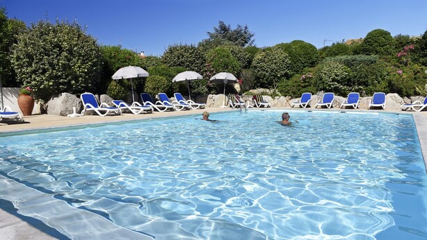 A swimming pool with clear water, surrounded by blue lounge chairs and umbrellas.