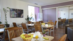 A dining area with wooden tables and chairs, breakfast items, and a large window with a view of the outside.