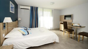 A hotel room with a bed, a desk, a chair, a TV, and a window with curtains.