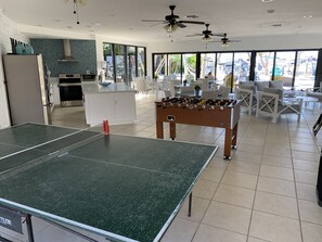 A spacious indoor area with a foosball table, a ping pong table, and a kitchen area with a refrigerator and oven. - Moon Bay 2 Bed Condo within B Building with side sea & pool views (Key Largo)