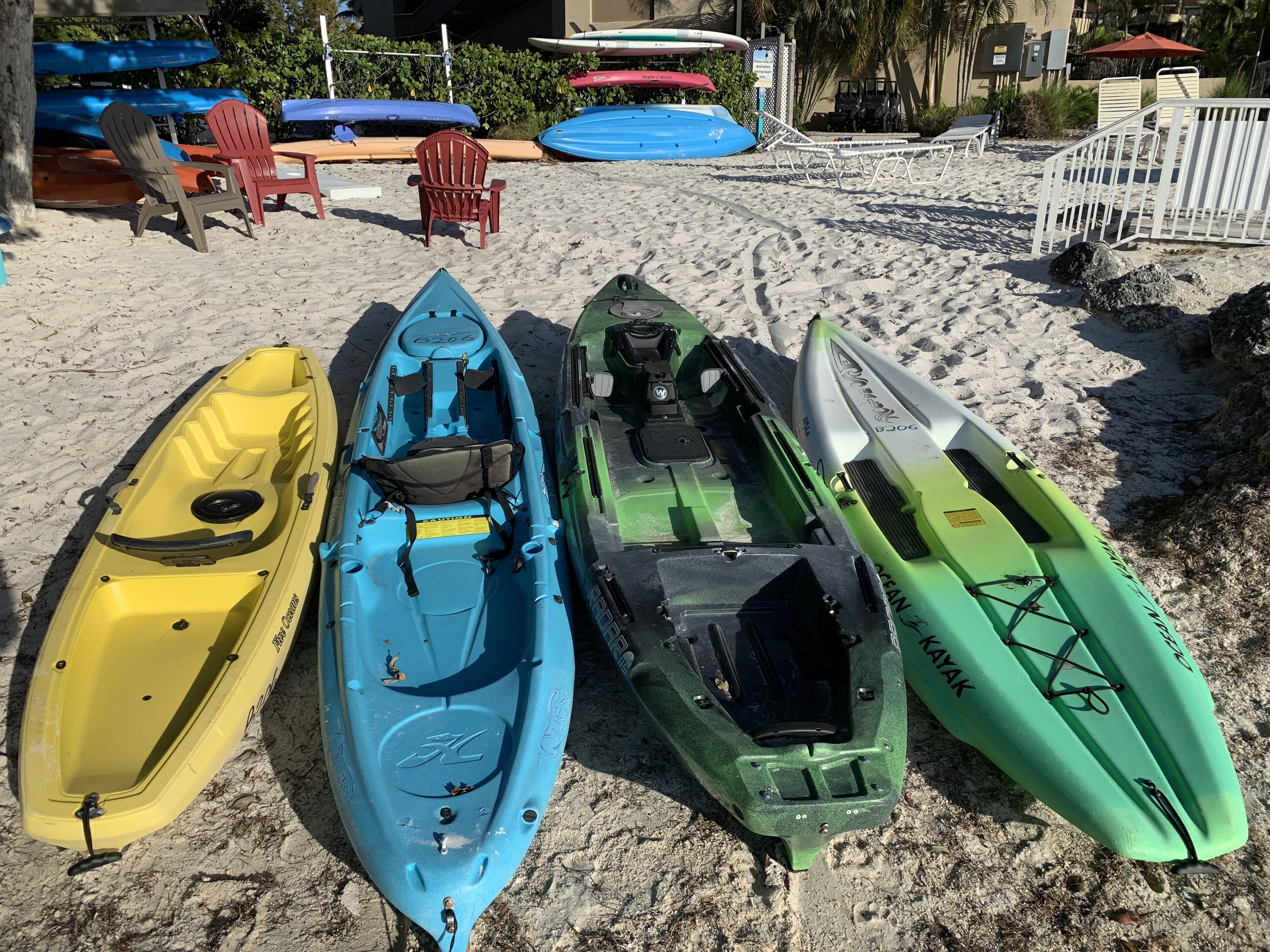 Kayaks lined up on a sandy beach with lounge chairs and umbrellas in the background.