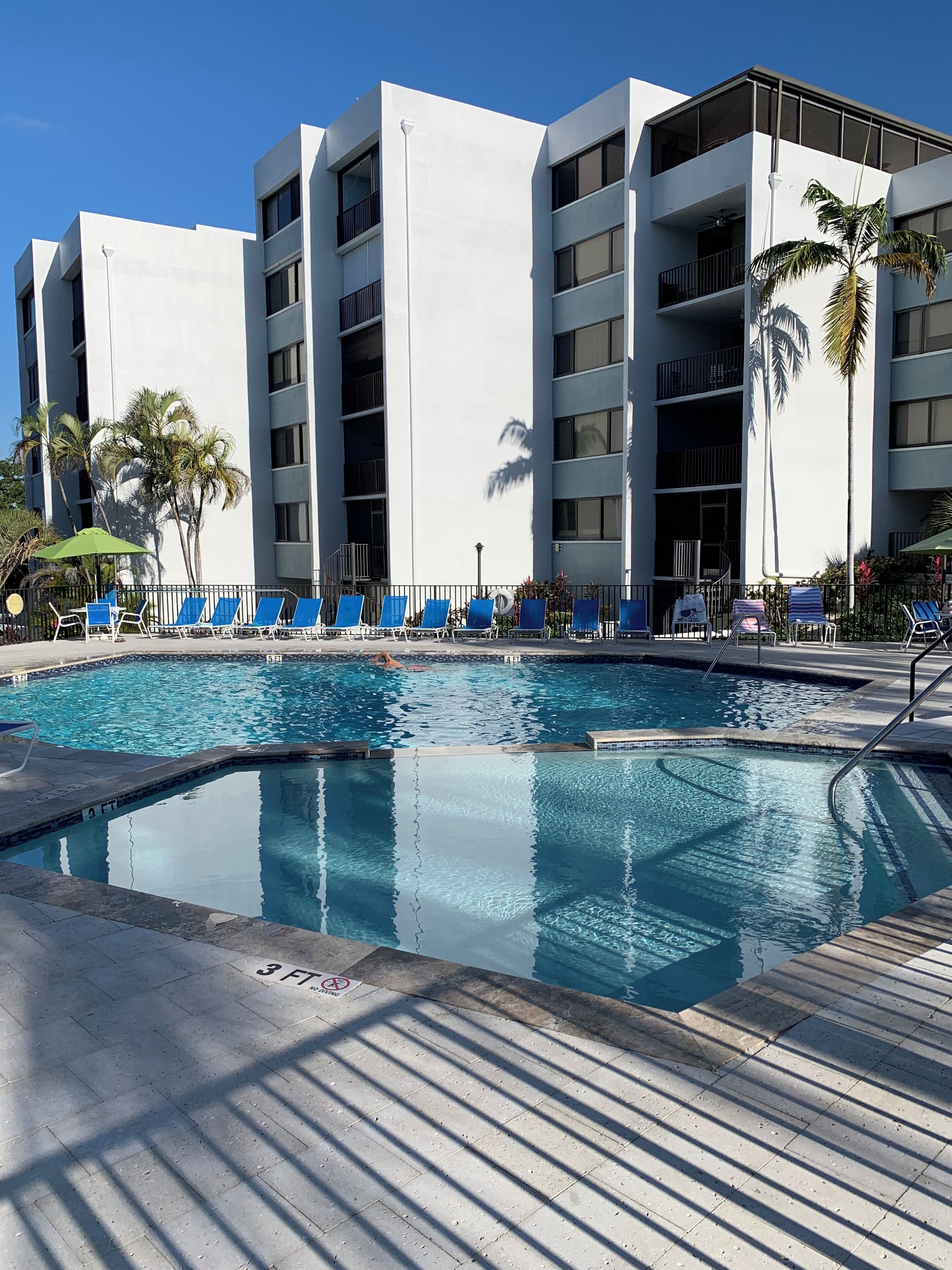 A modern building with a pool area, including lounge chairs and palm trees.