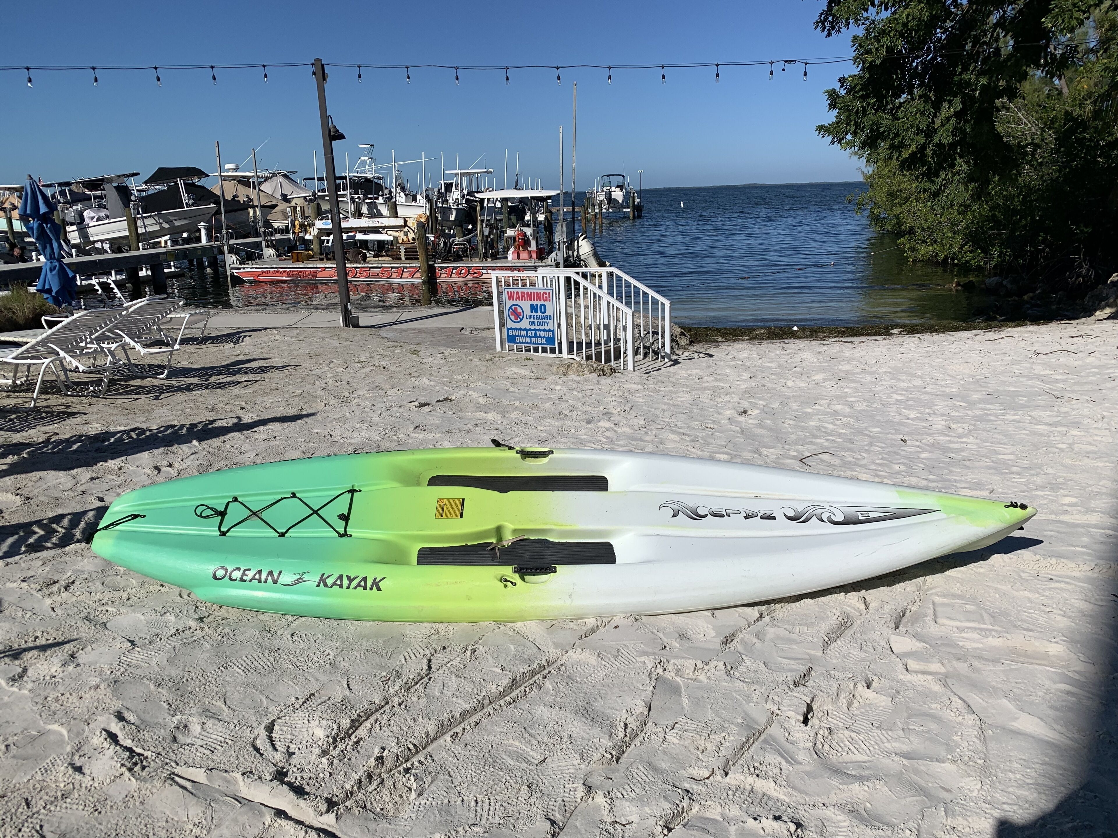 Ein Kajak an einem sandigen Strand, im Hintergrund Boote.