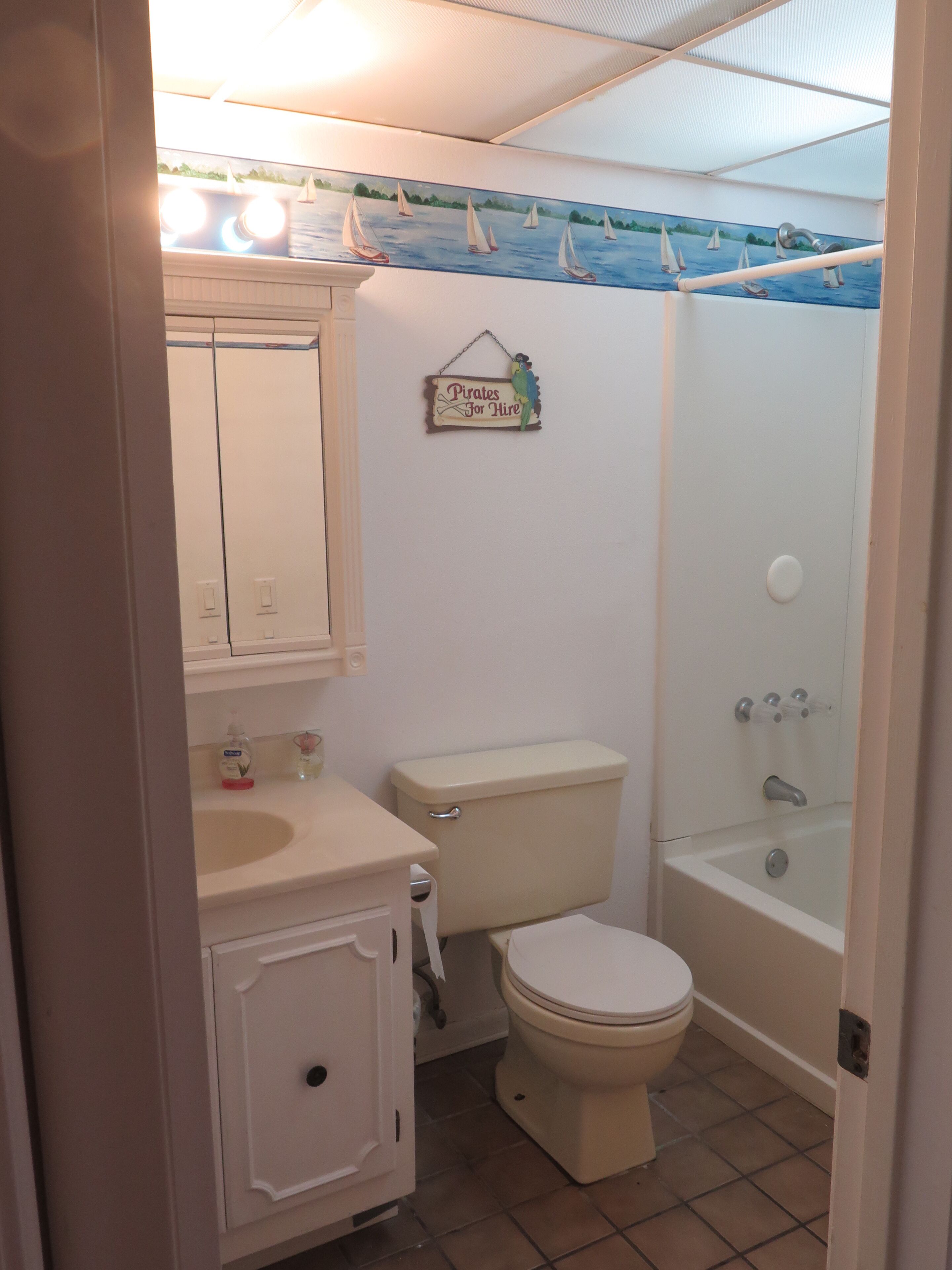 A bathroom with a toilet, sink, and shower. There is a sign on the wall that says "Pirates for Hire".