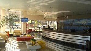 Un hall d’hôtel moderne doté d’un comptoir d’accueil, d’un espace salon et de grandes fenêtres offrant une vue sur le paysage urbain.