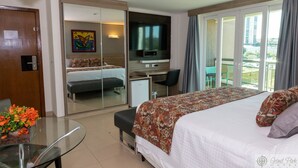 Une chambre d’hôtel avec un lit, un bureau, une télévision, un balcon avec vue et une table en verre décorée de fleurs.