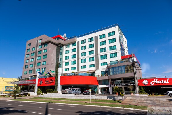 A hotel with multiple floors, a red and white facade, and a parking area in front. - Grand Park Hotel (Campo Grande)