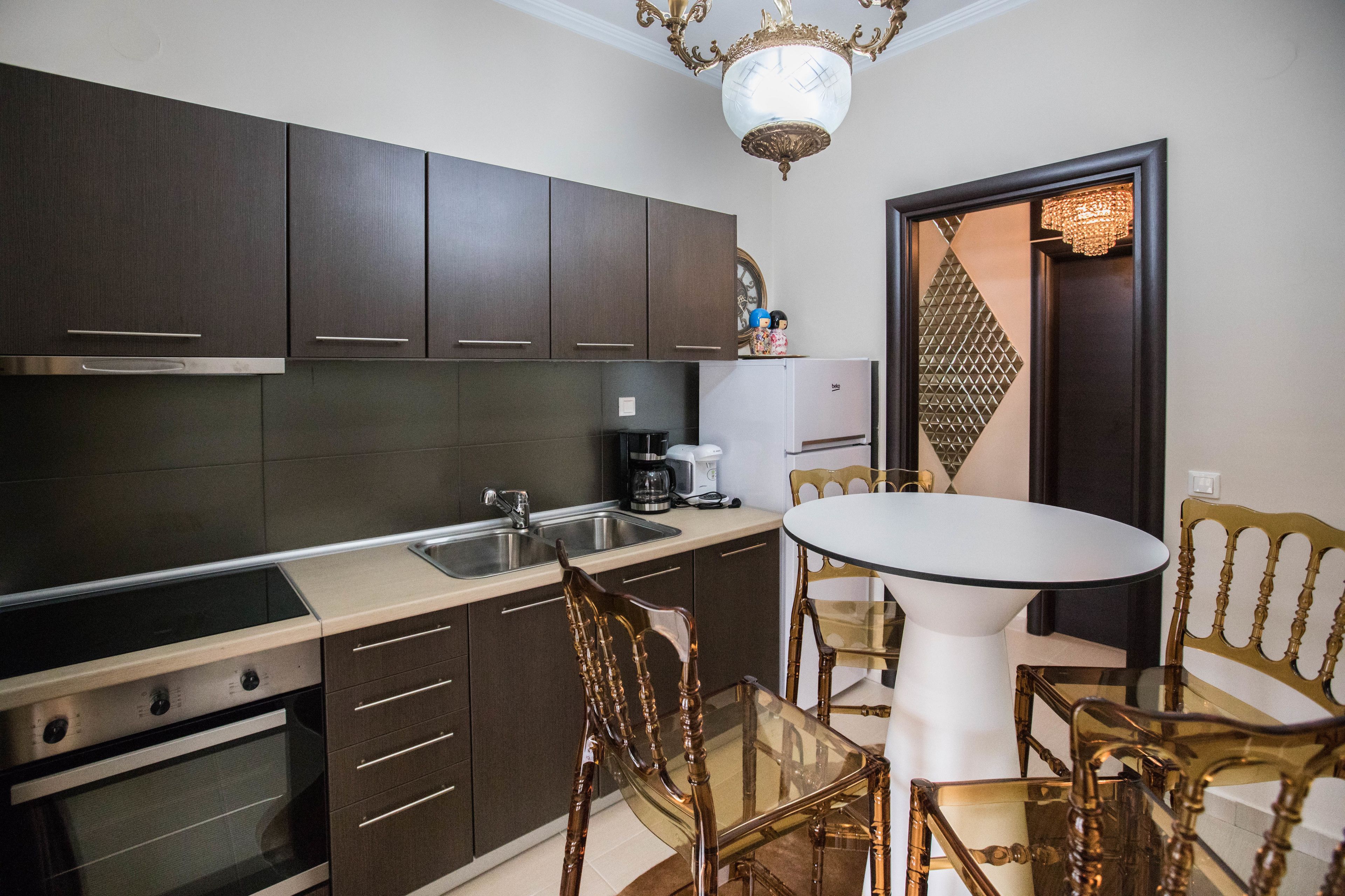 A compact kitchen with dark cabinets, a built-in oven, a sink, and a dining area with a glass table and wooden chairs.