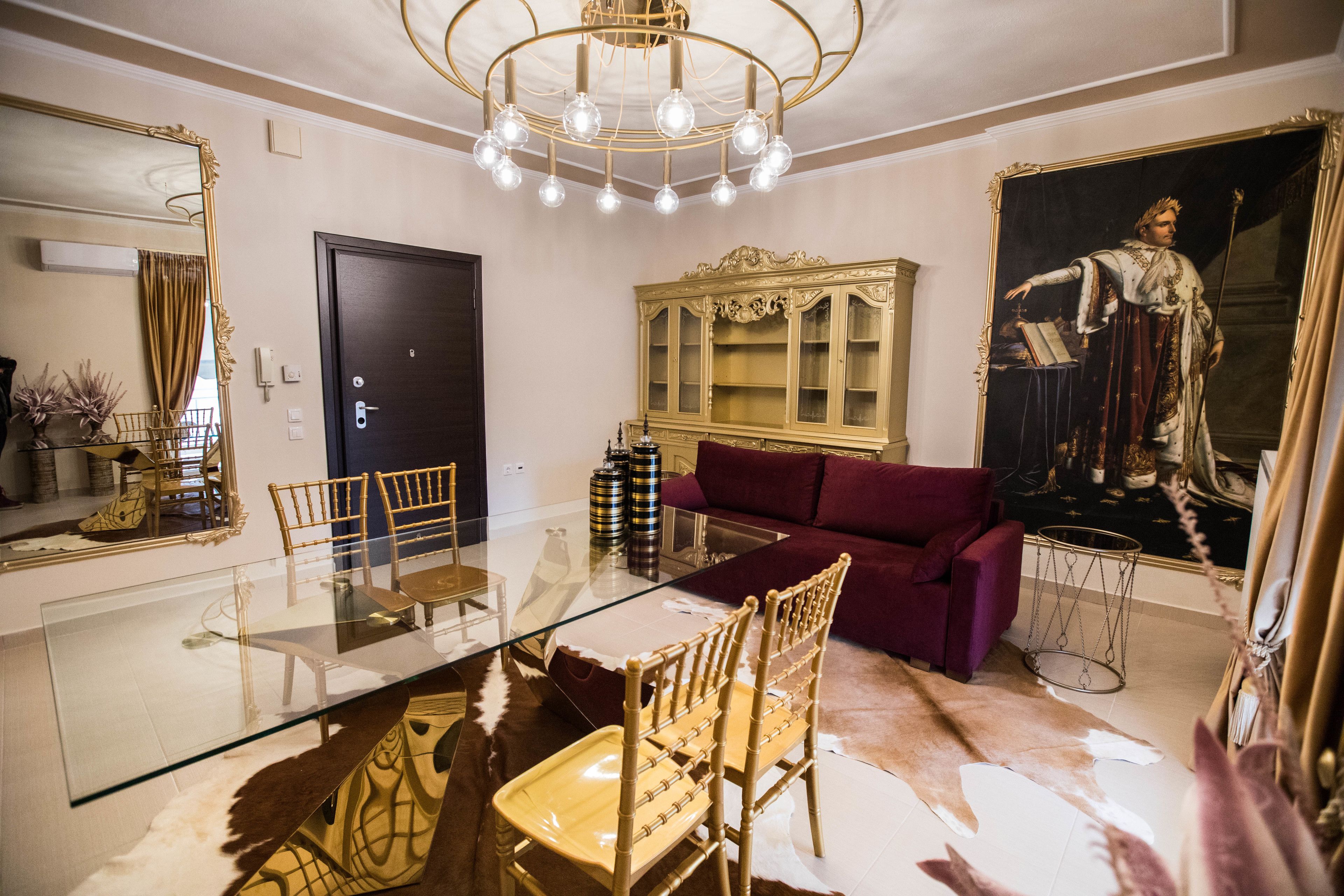 A dining area with a glass table, wooden chairs, a red sofa, and a large painting on the wall.