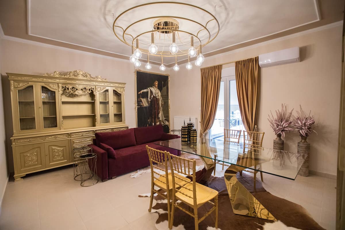 Ein Wohnzimmer mit einem Glastisch, einem roten Sofa, einem Holzstuhl, einem Dekioskabinett und einer Chandelüster.