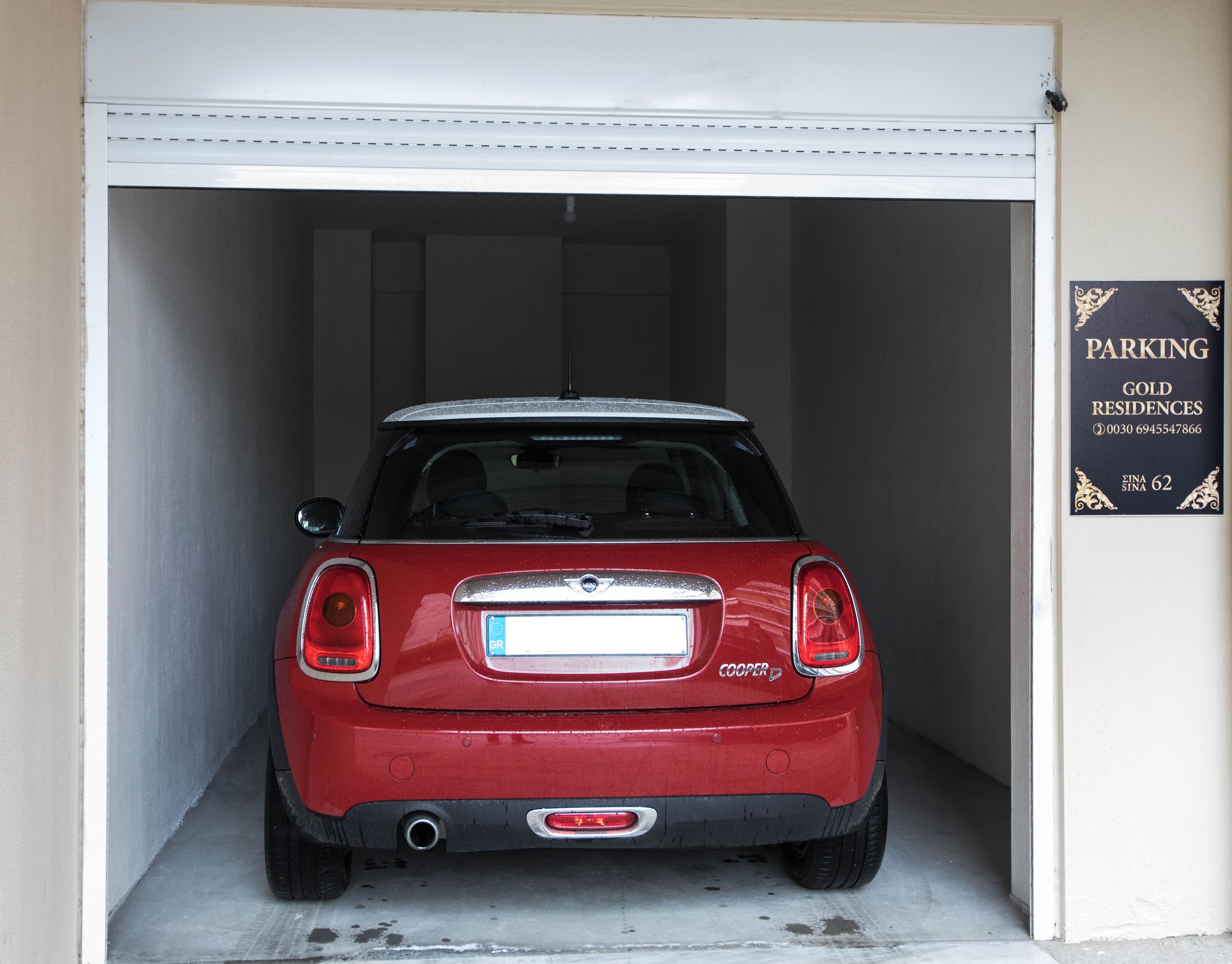 A red Mini Cooper parked inside a garage with a sign on the wall advertising 'PARKING GOLD RESIDENCES'.