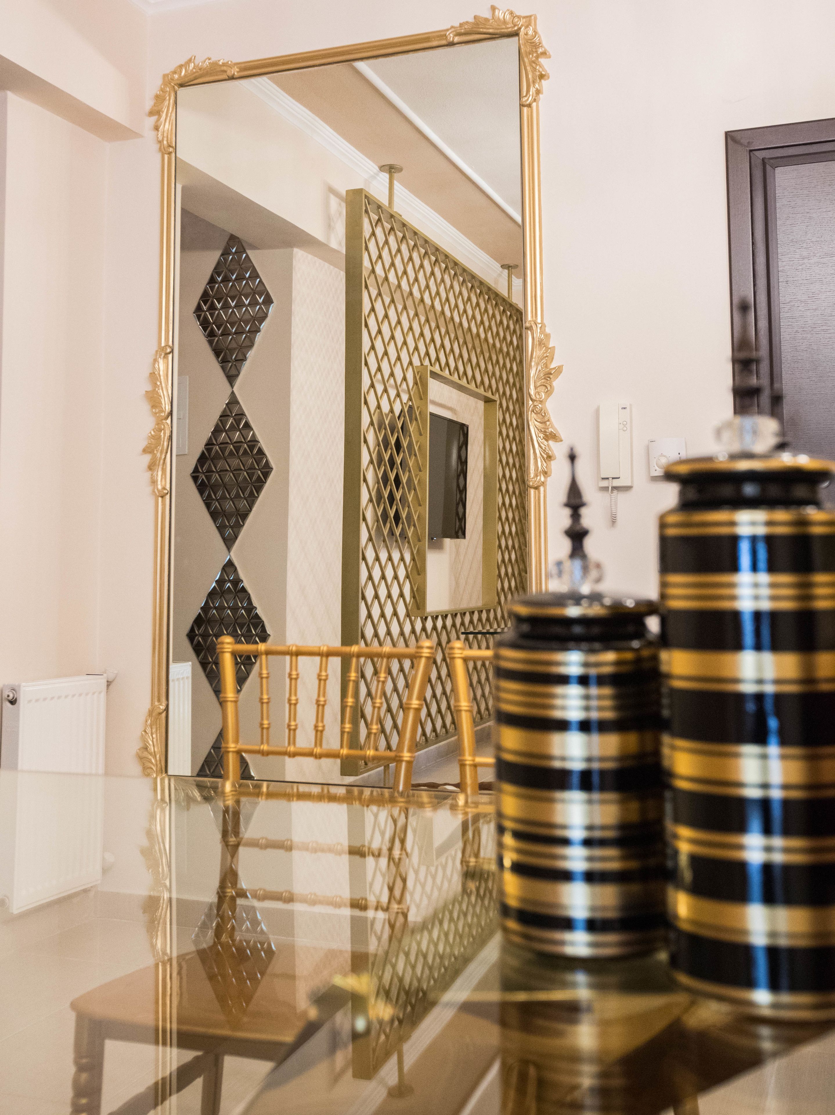 A room with a glass table, a gold-framed mirror, a decorative screen, and striped vases.