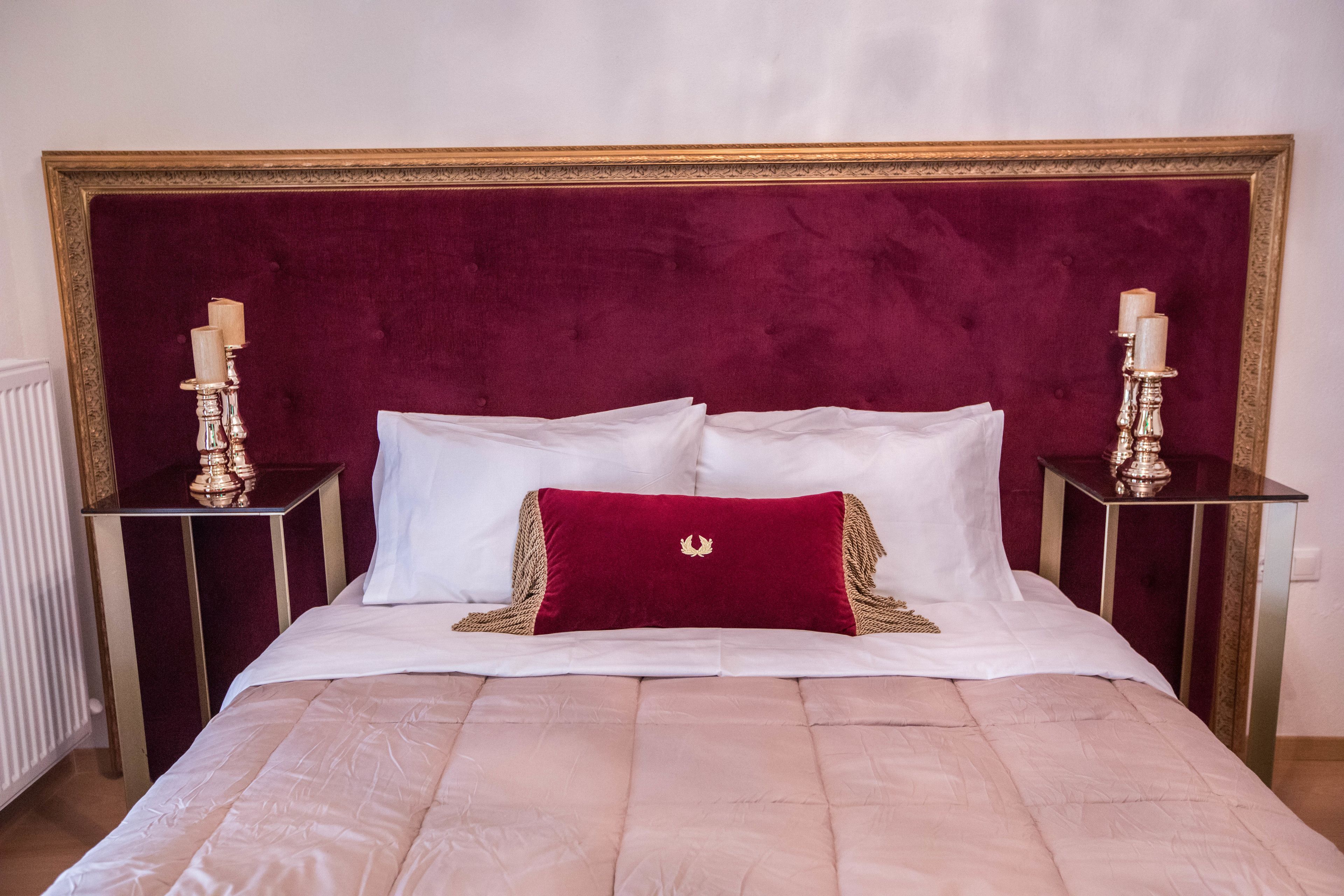 A bed with a red velvet headboard, white bedding, and two bedside tables with candles.