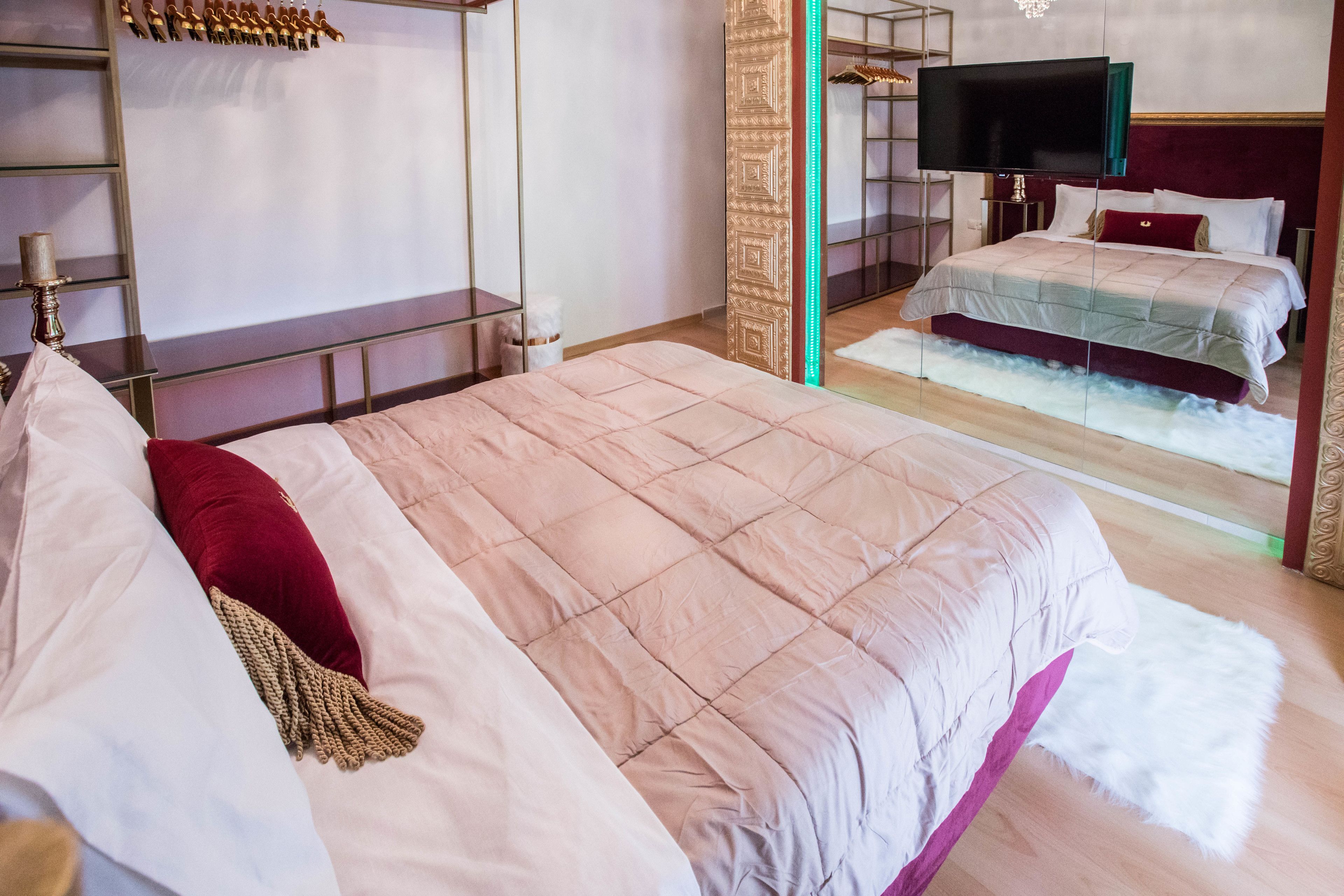 A hotel room with a large bed, a television, a mirror, and a wardrobe.