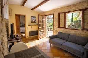 A room with a stone wall, a grey sofa, a wooden table with a laptop, and a view of greenery outside.