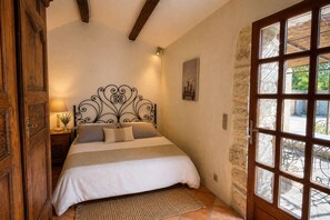 A bedroom with a bed, a nightstand, a lamp, a stone wall, and a window with a view. - Suite Margot, charming cottage for couples with swimming pool (Carnas)