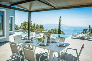 Zona pranzo con tavolo imbandito per sei persone, con vista su piscina e mare.