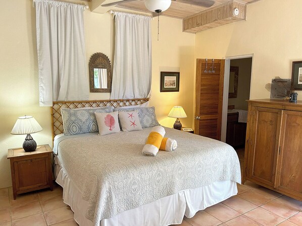 Une chambre à coucher comprenant un lit, des tables de chevet, une armoire et un ventilateur de plafond.