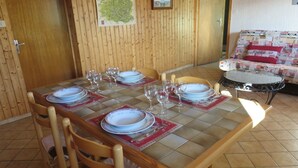 A dining table set with plates and glasses, wooden chairs, a small round table, and a wall-mounted map. - Appt in chalet in the heart of the Vosges balloons (Cornimont)
