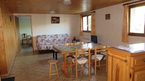 A cozy cabin interior with a wooden dining table, chairs, a sofa, and a television. - Appt in chalet in the heart of the Vosges balloons (Cornimont)