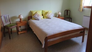 A bedroom with a wooden bed, two bedside tables with lamps, a chair, and a framed picture on the wall. - Appt in chalet in the heart of the Vosges balloons (Cornimont)