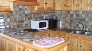 A kitchen with wooden cabinets, a microwave, a toaster, and a sink. - Appt in chalet in the heart of the Vosges balloons (Cornimont)