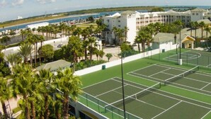 Ein Tennisplatz, umgeben von Palmen und einem mehrstöckigen Gebäude.