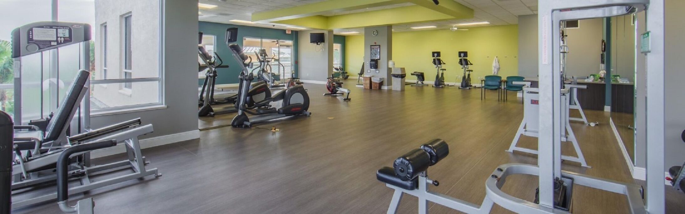 A gym with cardio machines, weight stations, and a mirror.